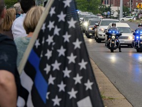A bystander displays a "Thin Blue Line" flag as the vehicle bearing the body of Calloway County Deputy Jody Cash proceeds to the Murray City Cemetery following Cash's memorial service in Murray, Ky., Saturday, May 21, 2022.