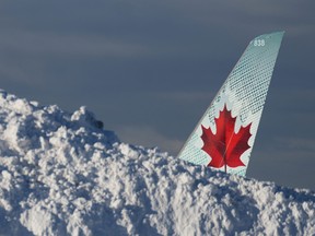 The tail of an Air Canada aircraft is seen behind a pile of snow at Vancouver International Airport in Richmond, B.C., Wednesday, Dec. 21, 2022.