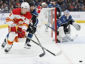 Calgary Flames' Mikael Backlund, left, and Columbus Blue Jackets' Boone Jenner chase the puck as Blue Jackets' Joonas Korpisalo (70) protects the net during the first period of an NHL hockey game on Friday, Dec. 9, 2022, in Columbus, Ohio.
