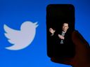 A phone screen displays a photo of Elon Musk with the Twitter logo shown in the background. 