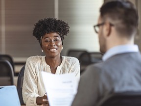 Beautiful young woman smiling during job interview while man, seen from behind, looks at resume.