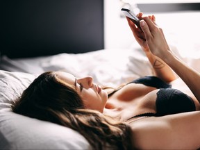 Beautiful young woman in lingerie reading text message on her mobile phone in bedroom.