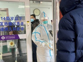 People line up next to a medical worker in a protective suit, at a fever clinic of a hospital amid the COVID-19 outbreak in Beijing, Dec. 15, 2022