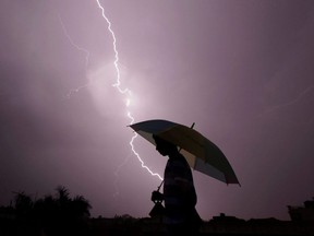 In this file photo taken May 15, 2015, a pedestrian walks with an umbrella as lightning strikes during an evening thunderstorm in Jammu, India.