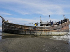Villagers look at a wooden boat used by Rohingya people in Pidie, Aceh province, Indonesia, Tuesday, Dec. 27, 2022.