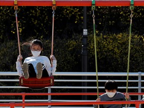 Children wearing masks following the rise in confirmed cases of COVID-19, play on the swings at a park in Daegu, South Korea, March 14, 2020.
