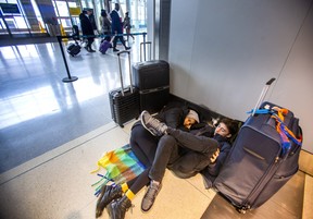 Aisha Osman (left) and Dean Fellner who are headed to Los Angeles, use their luggage to carve out a space to get some rest at Terminal 1 departures level at Toronto Pearson International Airport on Friday, Dec. 23, 2022.