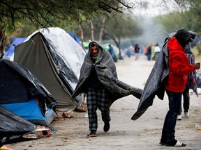 An asylum-seeking migrant walks covered with a blanket during a day of high winds and low temperatures at a makeshift encampment near the border between the U.S. and Mexico, after the U.S. Supreme Court allowed Title 42 to remain in place temporarily, in Matamoros, Mexico, on Dec. 23, 2022.
