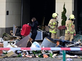 A woman who is not a hotel guest carries a suitcase past first responders standing amidst the debris in front of the Radisson Blu hotel, where a huge aquarium located in the hotel's lobby burst on Dec. 16, 2022 in Berlin.