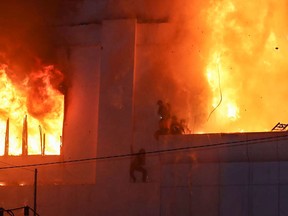 Fire burns around people on a ledge of the Grand on the side Diamond City hotel-casino in Poipet on December 29, 2022.