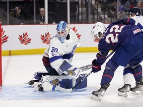 Finland goaltender Aku Koskenvuo watches the puck slide into the net as does the USA's Sam Lipkin during second period IIHF World Junior Hockey Championship action in Moncton, N.B., Saturday, Dec. 31, 2022.