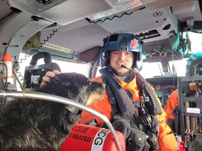 An unidentified member of the United States Coast Guard Air Station Port Angeles aircrew pets a dog on board his helicopter after the dog was airlifted from a sailboat that had washed onto rocks off Vancouver Island in a Wednesday, Dec. 28, 2022, handout photo.