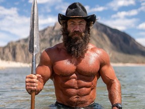 Bodybuilder wearing hat in water holding a giant spear.