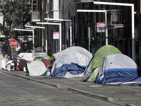 A man stands next to tents on a sidewalk in San Francisco on April 21, 2020.