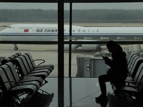 A passenger checks her phone as an Air China passenger jet taxi past at the Beijing Capital International airport in Beijing, Oct. 29, 2022.