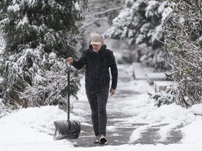 A man clears the sidewalk trying to keep ahead of the falling snow in Vancouver, Dec., 18, 2022.