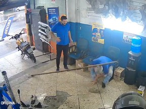 A screenshot of a viral video uploaded to twitter by @idososfzdmerda on January 10, a man is hit twice by a metal bar in car shop in Brazil. The bar was supposed to be supporting a door, but it slipped both times. Twitter/@idososfzdmerda