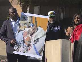 In this photo provided by WREG, Tyre Nichols' stepfather Rodney Wells, center, stands next to a photo of Nichols in the hospital after his arrest, during a protest in Memphis, Tenn., Saturday, Jan. 14, 2023.