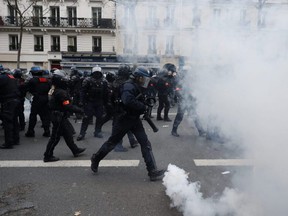 Riot police officers run through tear gas during a demonstration against pension changes, in Paris, Thursday, Jan. 19, 2023.