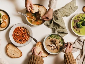 People eating Autumn and Winter creamy vegan soups, fall and winter vegetarian food menu. Flat-lay of peoples hands eating homemade soup with fresh bread over white table background, top view