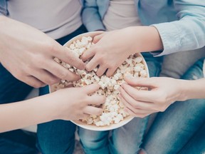Top view close up portrait of hands taking sweet pop corn from bucket, dad mom kids sharing popcorn while watching film program tv, sitting on sofa indoor, enjoying free time having fun