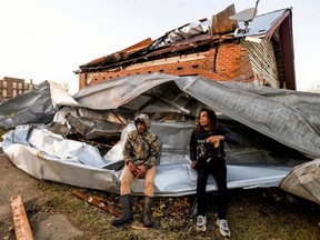 Cordel Tyus and Devo McGraw sit on roofing that blew off of an industrial building and wrapped around their house after a tornado ripped through Selma, Alabama, Jan. 12, 2023.