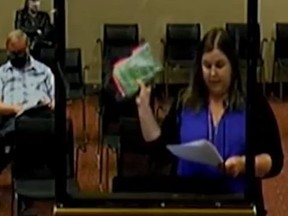 Screen shot of mom holding up book during school board meeting.