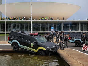 In this file photo taken on January 8, 2023, members of the Federal Legislative Police stand next a vehicle that crashed into a fountain as supporters of Brazilian former President Jair Bolsonaro invade the National Congress in Brasilia.
