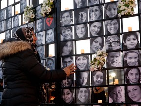 In this file photo taken on Jan. 8, 2022, a woman touches victims' portraits as mourners attend an outdoor vigil for the victims of Ukrainian passenger jet flight PS752, which was shot down two years ago over Iran, in Toronto.