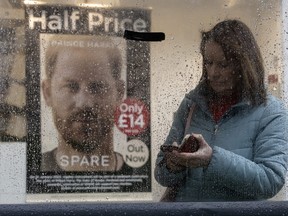 A woman waits under a bus shelter in the rain as Prince Harry's book "Spare" goes on display in a branch of WH Smith opposite Windsor Castle on Jan. 10, 2023 in Windsor, England.