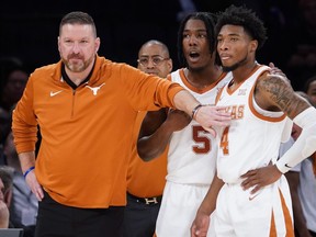 Texas' head coach Chris Beard, left, meets with Tyrese Hunter (4) and Marcus Carr (5) at the bench during the first half of the team's NCAA college basketball game against Illinois in the Jimmy V Classic, Tuesday, Dec. 6, 2022, in New York.