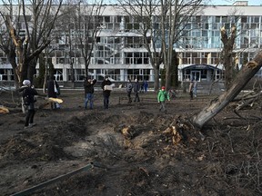 Bystanders look at a crater next to an educational building in Kyiv on January 1, 2023, which was damaged by a missile strike on the previous day, amid the Russian invasion of Ukraine.