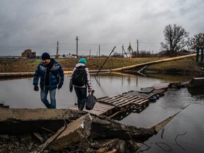 Local residents cross a makeshift pontoon made of wooden pallets alongside a destroyed bridge in Bakhmut, Donetsk region, on January 6, 2023.