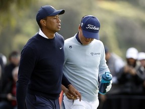 Tiger Woods hands Justin Thomas an item believed to be a tampon as they walk off the ninth tee during the first round of the The Genesis Invitational at Riviera Country Club on February 16, 2023 in Pacific Palisades, California.