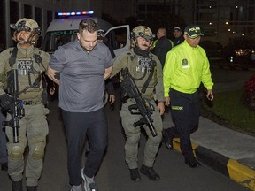 This photo released by the Colombian prosecutor's press office shows members of the police guarding U.S. John Nelson Poulos, a suspect in the murder of his girlfriend, in Bogota on January 26, 2023. - A U.S. citizen suspected of the murder in Bogota of his girlfriend, a popular Colombian DJ, has been deported from Panama and will remain in custody while his prosecution progresses, the Colombian prosecutor's office reported Thursday.