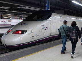 Passengers walk past an AVE high-speed train at Barcelona-Sants railway station prior to departing to Lyon on a test trip along a new international rail line between Spain and France, in Barcelona on February 13, 2023.