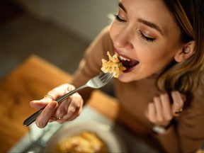 Close-up of young happy woman eating pasta at dining table.