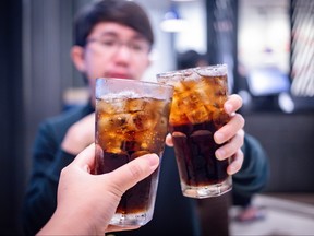 Two glasses of cola with ice with young man in background.