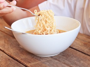 Child eating instant noodles in white bowl on wooden table.