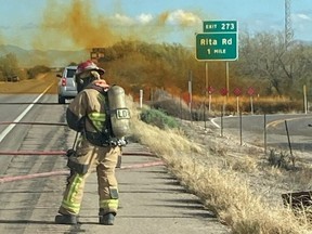 A firefighter works as an overturned truck spews orange smoke in the background at I-10 Highway in Tucson, Ariz., Tuesday, Feb. 14, 2023.