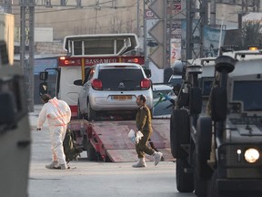 Israeli security forces block a road while others tow a car at the site of an attack in which two Israelis were killed in Hawara town, in the occupied West Bank on February 26, 2023.