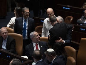 Israel's Prime Minister Benjamin Netanyahu, center, and lawmakers congratulate Justice Minister Yariv Levin, back to camera, after his speech in Israel's parliament, the Knesset, just before a vote on a contentious plan to overhaul the country's legal system, in Jerusalem, early Tuesday, Feb. 21, 2023.