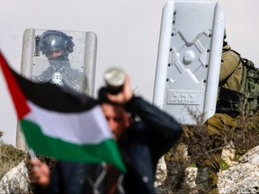 A Palestinian protester waves a flag near the Israeli security forces during a demonstration against the Israeli outposts in the occupied West Bank city of Nablus on Feb. 24, 2023.