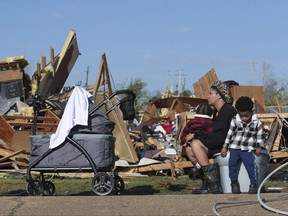 Melanie Childs of Amory, Miss., sits on a bucket and holds her two children, Mila, 1, left, and Major, 2, as they view whats left of her grandfather's home on March 25, 2023.