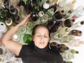 Young woman in jeans and t-shirt sitting on the floor with lots of empty beer bottles and is drunk.