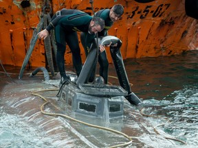 In this file photo taken on Nov. 26, 2019, Spanish Civil Guard divers stand over the refloated prow of a submarine used to transport drugs illegally in Aldan, northwestern Spain.