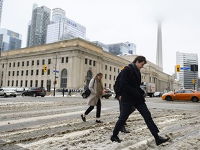 People walk through snow and slush on Bay Street following a winter storm that affected southern Ontario, in Toronto, on Thursday, Feb., 23, 2023. THE CANADIAN PRESS/Christopher Katsarov