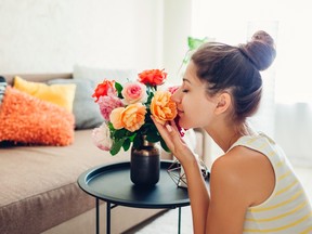 Woman smelling fresh roses in vase on table. Housewife taking care of coziness in apartment. Interior and decor