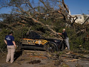 A law enforcement officer cuts a tree with a chainsaw to free a trapped police vehicle after thunderstorms spawning high straight-line winds and tornadoes ripped across the state in Rolling Fork, Mississippi, March 25, 2023.