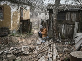 A woman keeps notes and uses her smartphone as she sits in the yard of a home in the town of Chasiv Yar, near Bakhmut, on March 24, 2023.